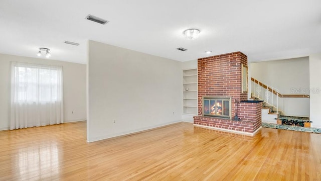 unfurnished living room featuring hardwood / wood-style flooring, built in features, and a fireplace