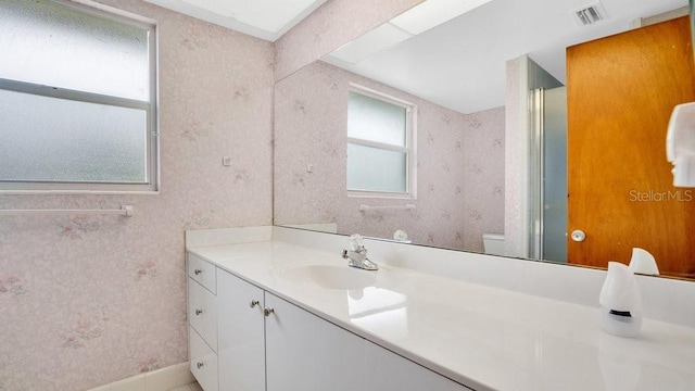 bathroom featuring a wealth of natural light, toilet, vanity, and walk in shower