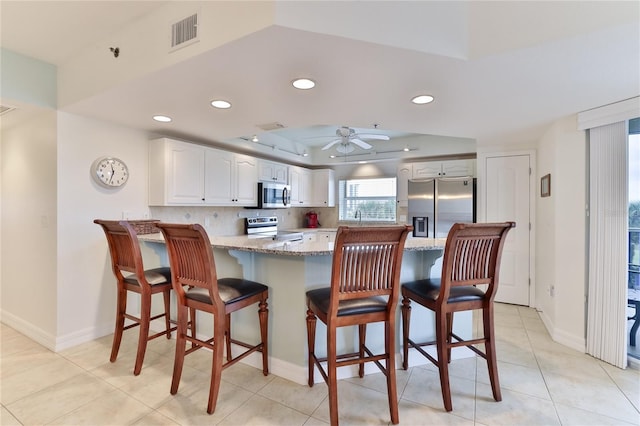 kitchen featuring light stone countertops, kitchen peninsula, stainless steel appliances, ceiling fan, and white cabinets