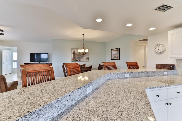 kitchen with a notable chandelier, a breakfast bar, light stone countertops, and white cabinetry