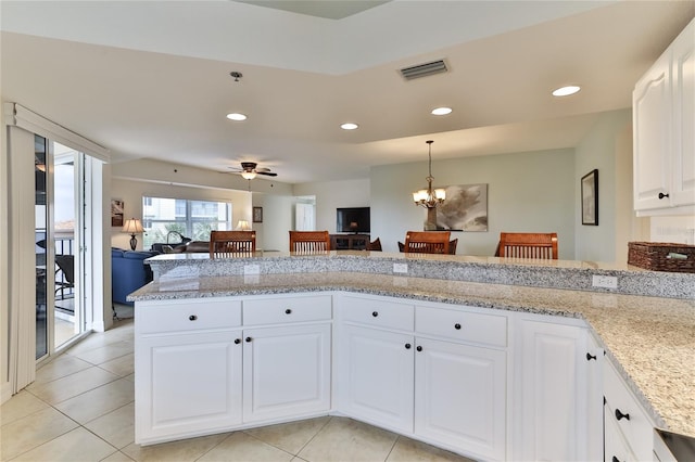 kitchen with light stone countertops, kitchen peninsula, pendant lighting, white cabinets, and ceiling fan with notable chandelier