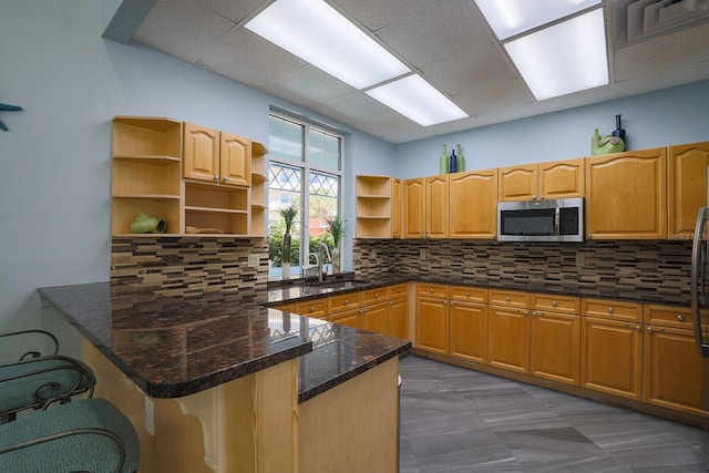 kitchen featuring kitchen peninsula, a paneled ceiling, tasteful backsplash, dark stone counters, and sink