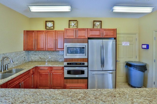 kitchen featuring backsplash, light stone countertops, sink, and stainless steel appliances