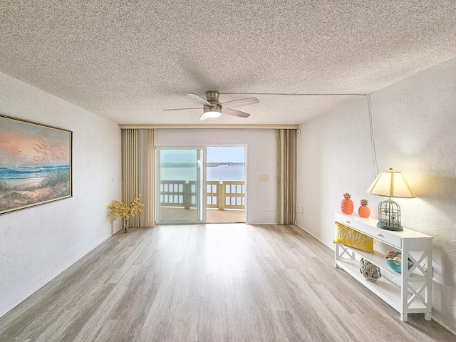 spare room with light wood-type flooring, a textured ceiling, a water view, and ceiling fan