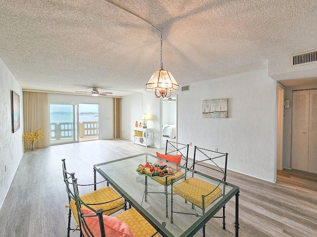 dining room featuring ceiling fan with notable chandelier, a textured ceiling, and hardwood / wood-style flooring