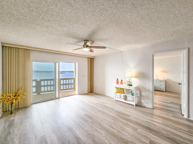 empty room with ceiling fan, a water view, light hardwood / wood-style floors, and a textured ceiling