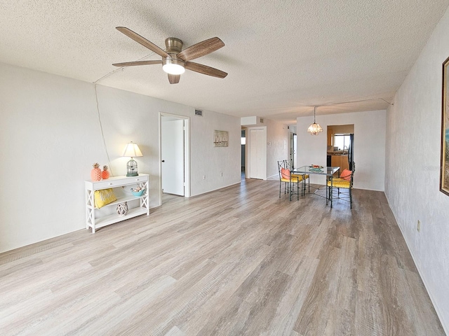 living area with ceiling fan with notable chandelier, a textured ceiling, and light hardwood / wood-style flooring