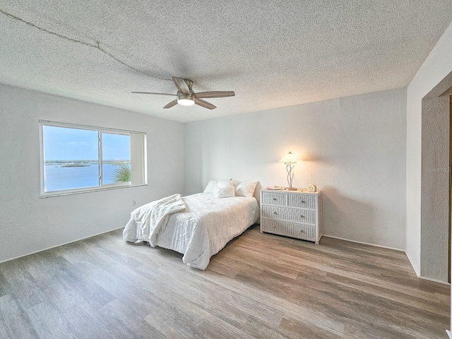 bedroom featuring a water view, wood-type flooring, and a textured ceiling