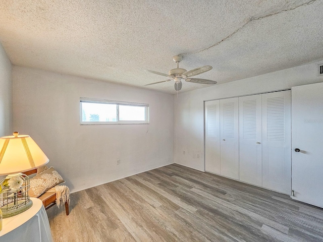 unfurnished bedroom featuring ceiling fan, wood-type flooring, a textured ceiling, and a closet