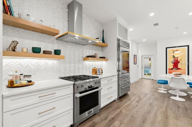 kitchen featuring white cabinetry, wall chimney exhaust hood, light hardwood / wood-style flooring, decorative light fixtures, and high end appliances