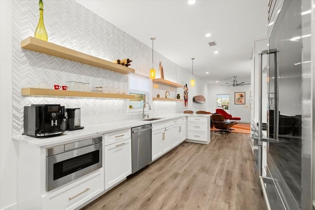 kitchen with sink, light hardwood / wood-style flooring, appliances with stainless steel finishes, decorative light fixtures, and white cabinetry