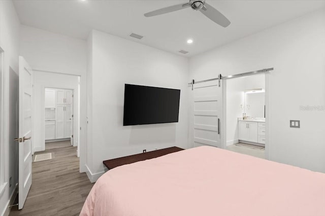 bedroom featuring hardwood / wood-style floors, a barn door, ensuite bath, and ceiling fan