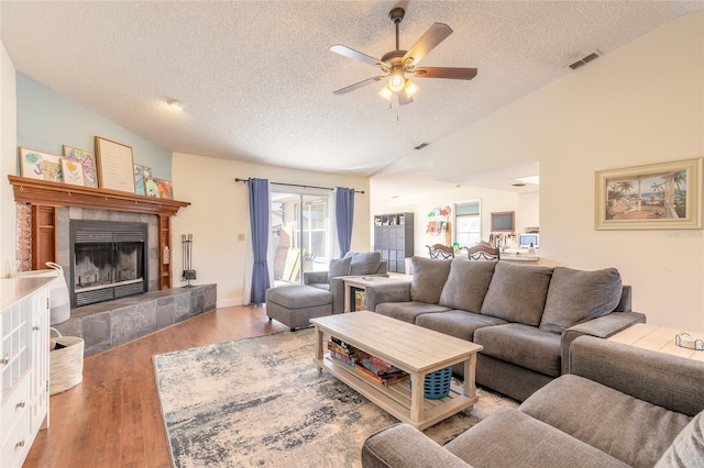 living room featuring vaulted ceiling, a fireplace, light hardwood / wood-style floors, and a textured ceiling