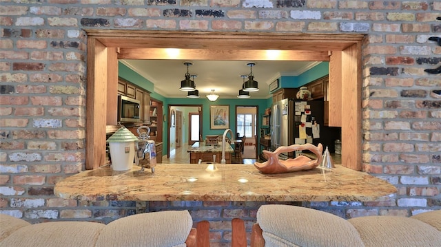 kitchen featuring sink, stainless steel appliances, brick wall, decorative light fixtures, and ornamental molding