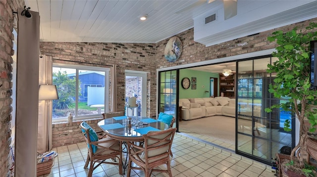 dining area with ceiling fan, light tile patterned floors, brick wall, and vaulted ceiling