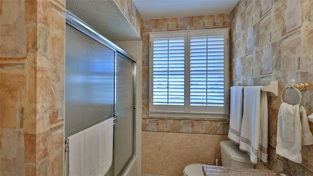 bathroom with enclosed tub / shower combo, tile walls, and toilet