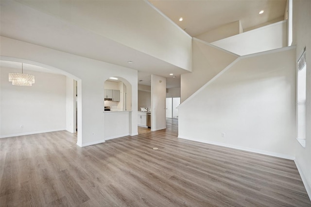 unfurnished living room with hardwood / wood-style floors, an inviting chandelier, and a high ceiling