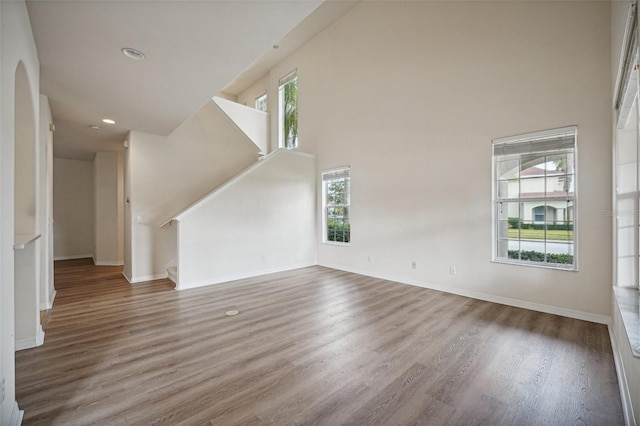 unfurnished living room featuring plenty of natural light, wood-type flooring, and a towering ceiling