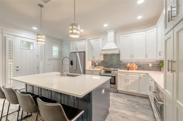 kitchen featuring appliances with stainless steel finishes, premium range hood, white cabinetry, and a center island with sink