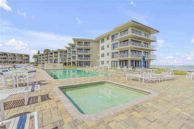 view of swimming pool with a community hot tub, a water view, and a patio