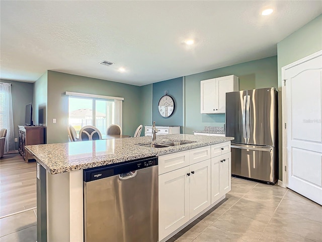 kitchen with appliances with stainless steel finishes, light stone counters, sink, a center island with sink, and white cabinets