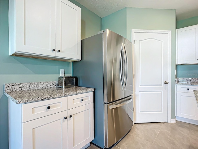 kitchen with stainless steel fridge, light stone counters, a textured ceiling, light tile patterned floors, and white cabinetry