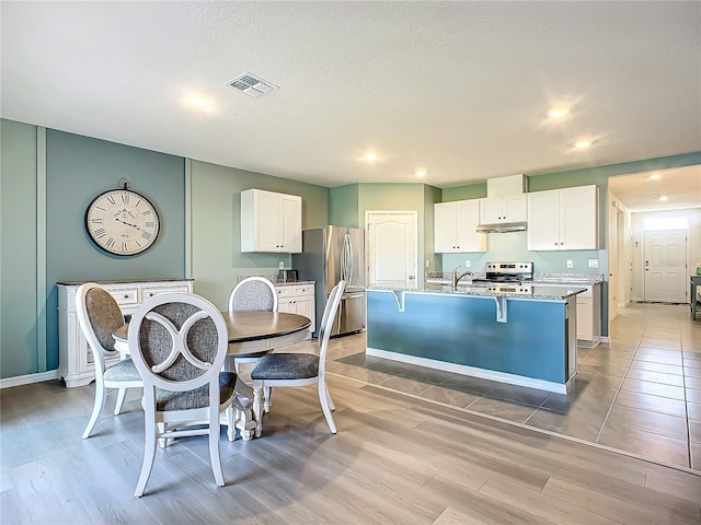 kitchen featuring a kitchen island with sink, white cabinets, stainless steel appliances, and light stone counters