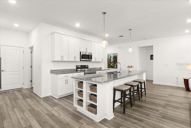 kitchen with stainless steel appliances, white cabinetry, and an island with sink