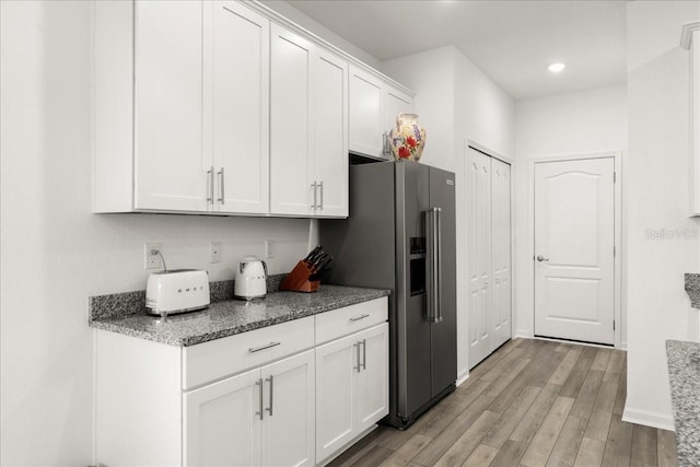 kitchen featuring high end refrigerator, light hardwood / wood-style flooring, white cabinetry, and dark stone countertops