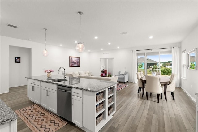 kitchen featuring light stone countertops, white cabinetry, sink, stainless steel dishwasher, and a center island with sink