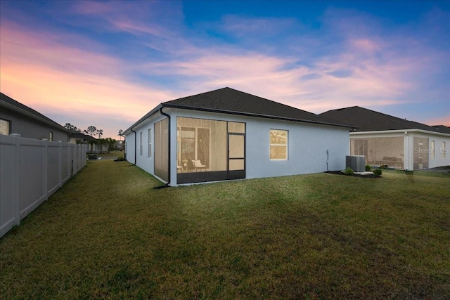 back house at dusk featuring a lawn and central air condition unit