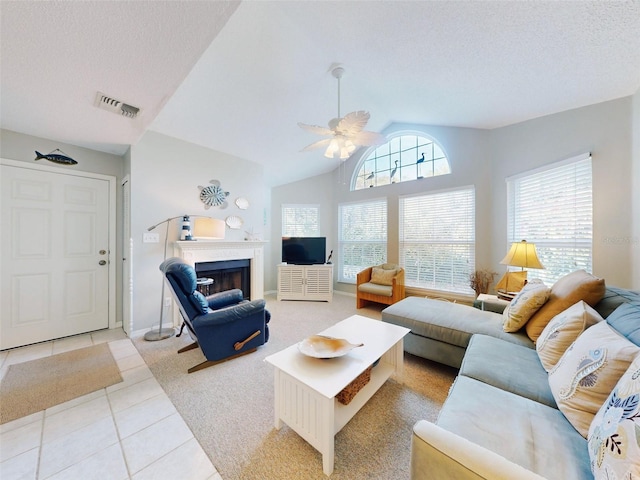 living area featuring a fireplace, visible vents, light tile patterned flooring, ceiling fan, and a textured ceiling