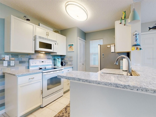 kitchen with white appliances, white cabinets, decorative backsplash, light stone counters, and a sink