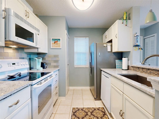 kitchen with light tile patterned floors, white appliances, a sink, white cabinets, and light stone countertops