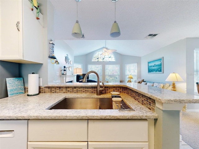 kitchen featuring lofted ceiling, light stone counters, open floor plan, pendant lighting, and a sink