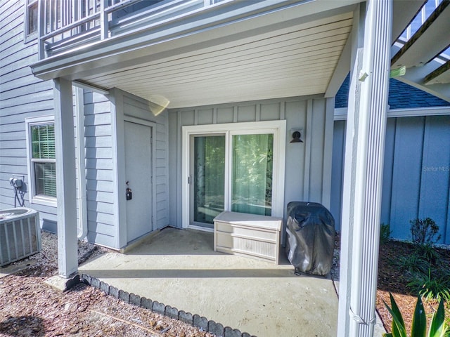 view of exterior entry with board and batten siding, cooling unit, and a balcony