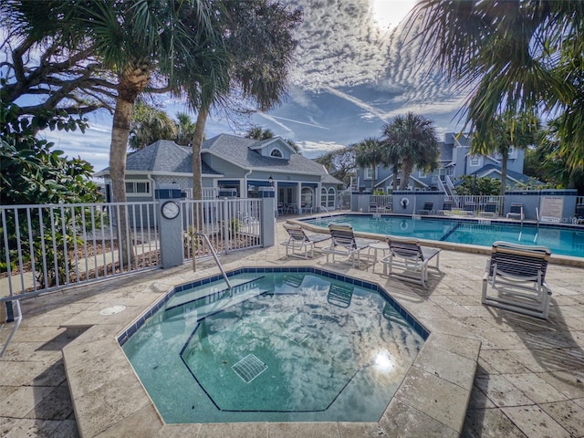 community pool with a patio, a hot tub, and fence