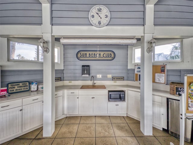 kitchen with white cabinets, stainless steel microwave, light countertops, a sink, and light tile patterned flooring