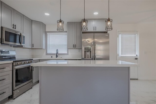 kitchen with sink, hanging light fixtures, gray cabinets, a kitchen island, and stainless steel appliances