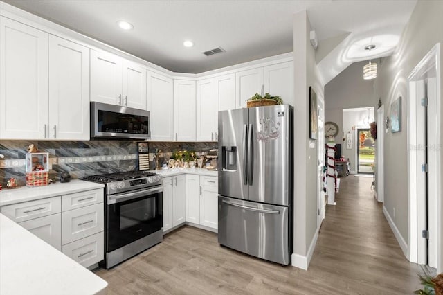 kitchen with white cabinets, hanging light fixtures, tasteful backsplash, light hardwood / wood-style floors, and stainless steel appliances