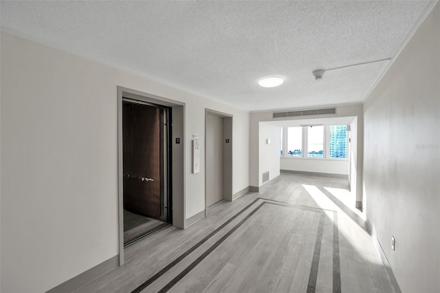 hallway featuring light hardwood / wood-style floors, a textured ceiling, and elevator