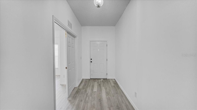 hall with light wood-type flooring and a textured ceiling