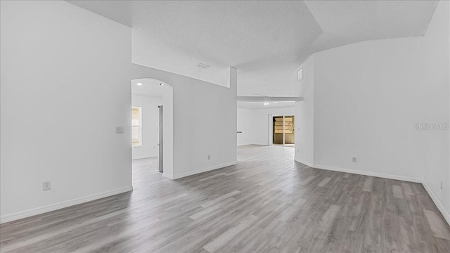 empty room featuring a textured ceiling, light hardwood / wood-style flooring, and lofted ceiling