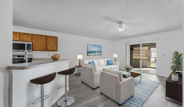 living room with a textured ceiling, light wood-type flooring, and ceiling fan