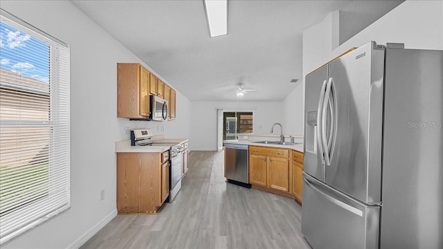 kitchen with kitchen peninsula, light wood-type flooring, stainless steel appliances, ceiling fan, and sink