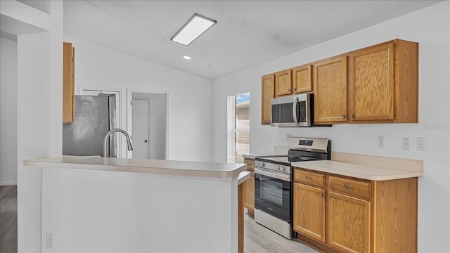 kitchen featuring appliances with stainless steel finishes, light wood-type flooring, a textured ceiling, sink, and lofted ceiling