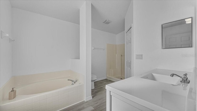 bathroom featuring tiled tub, vanity, wood-type flooring, and toilet