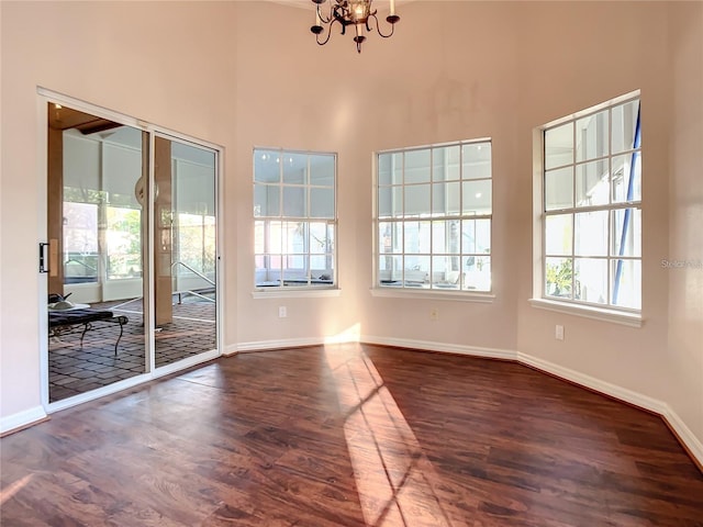 spare room with dark hardwood / wood-style flooring, a high ceiling, and an inviting chandelier