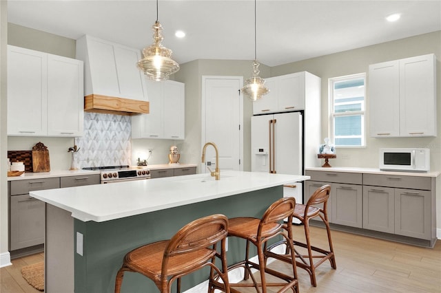 kitchen featuring gray cabinetry, white appliances, backsplash, sink, and an island with sink