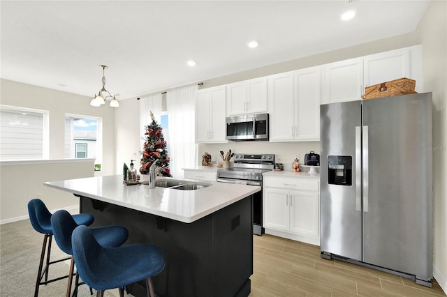 kitchen featuring white cabinetry, sink, decorative light fixtures, a center island with sink, and appliances with stainless steel finishes